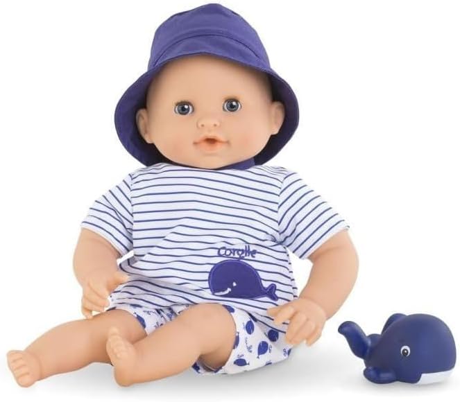 The Corolle Bebe Bath Doll, wearing a purple hat and striped shirt with a whale print, sits beside a blue toy whale—an adorable water-play companion, shown against a white background.