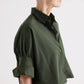 A person with short gray hair wears the TWP Next Ex Superfine Cotton Shirt in Rosen Green, a loose-fitting, cropped, short-sleeve button-down with rolled-up sleeves, shown from the side against a plain background.