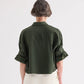 A person with short gray hair faces away from the camera, wearing the TWP Next Ex Superfine Cotton Shirt in Rosen Green and light-colored pants.