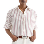 A person wearing the TWP Next Ex Stripe Shirt—an airy cotton-silk-blend, cropped short-sleeve button-down featuring red vertical stripes and rolled sleeves—paired with white pants and a brown belt.