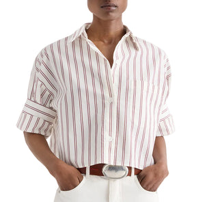 A person wearing the TWP Next Ex Stripe Shirt—an airy cotton-silk-blend, cropped short-sleeve button-down featuring red vertical stripes and rolled sleeves—paired with white pants and a brown belt.