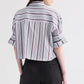 A person stands with their back to the camera, wearing TWP’s Next Ex Striped Superfine Poplin Shirt and black pants against a plain background.