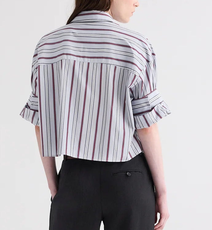 A person stands with their back to the camera, wearing TWP’s Next Ex Striped Superfine Poplin Shirt and black pants against a plain background.