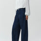 A person wears the Simkhai Frida Top, a white long-sleeve silk georgette blouse with pleats and blouson sleeves, paired with wide-leg dark blue jeans, standing against a plain light background.