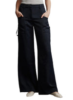 A person wearing TWP Chrystie Pant in black, styled with wide legs and side pockets, has their hands comfortably tucked in while paired with beige shoes.