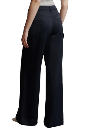 A person is seen from the back wearing TWP's black Chrystie Pant, designed with wide-leg cargo styling in coated viscose and linen, paired with a light-colored top.