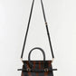 The Simkhai River Small Top Handle Bag is styled in a bold black and brown tiger-print pattern, enhanced by gold hardware and a long adjustable crossbody strap, and is displayed against a plain light background.