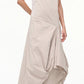 A woman wearing the Staud Viola Dress—sleeveless with a draped skirt and asymmetrical hem—pairs it with pointed-toe snakeskin flats while standing against a plain white background.