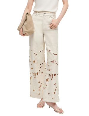 A person wearing Simkhai's Betty Floral Cut Out Jeans, a white sleeveless top, heeled sandals, and holding a beige clutch.