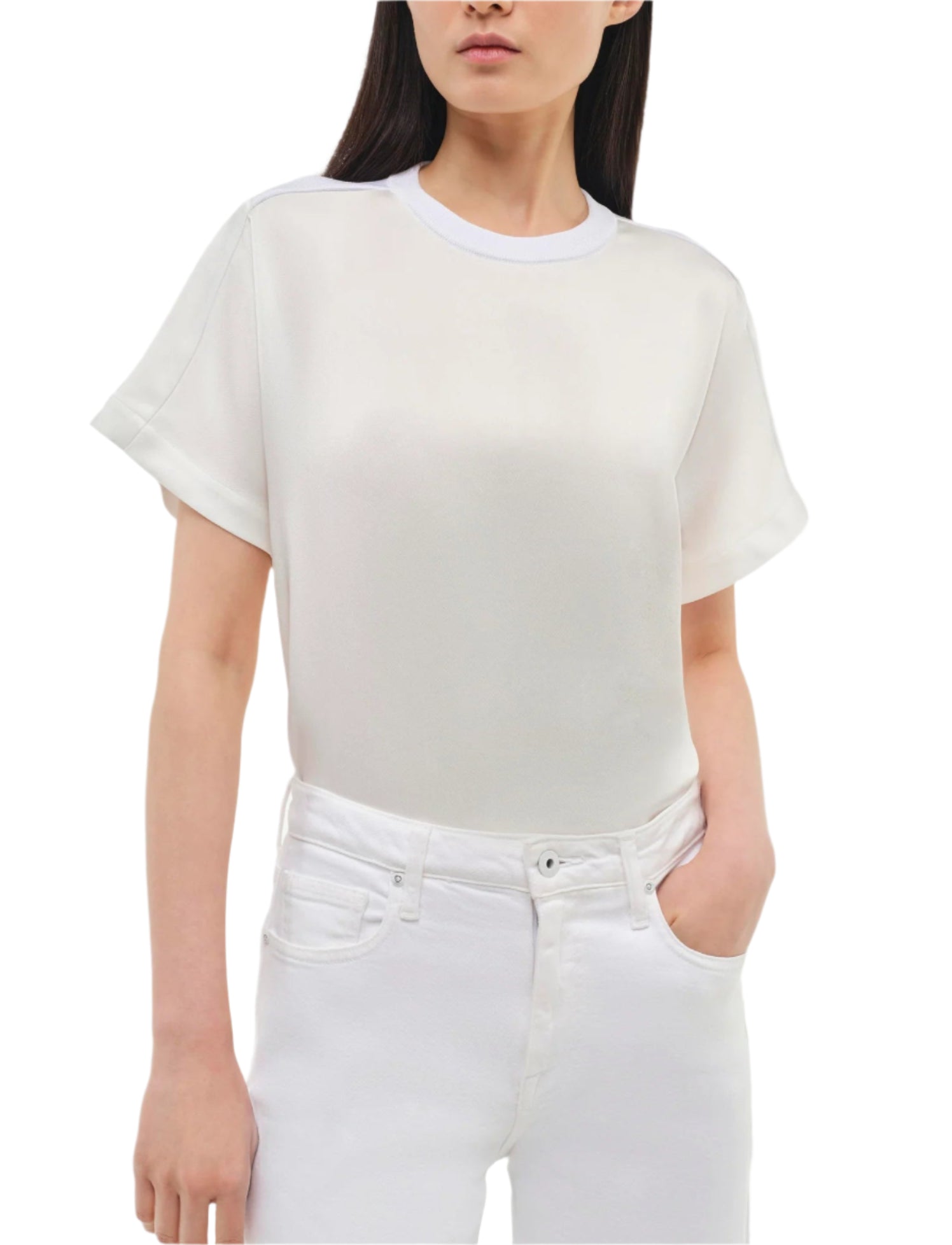 A woman wears the Simkhai Addy Satin T-Shirt—a plain white, relaxed-fit short-sleeve top with a round neckline—paired with white jeans and stands with one hand in her pocket.