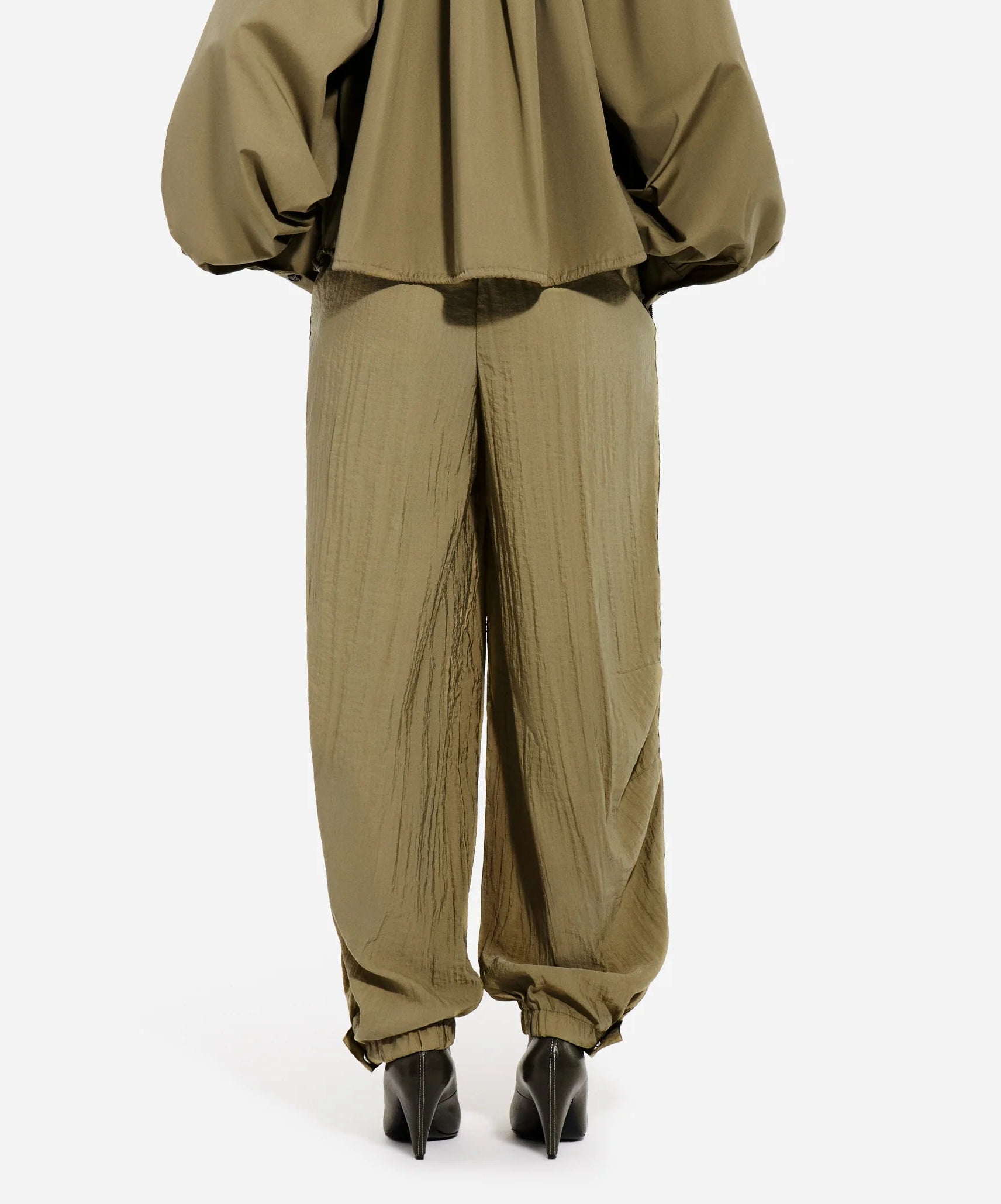 Model wears CO’s Articulated Vented Pant in olive with an elastic waist, styled with a matching oversized top and black pointed heels, shown from the back against a plain white background.