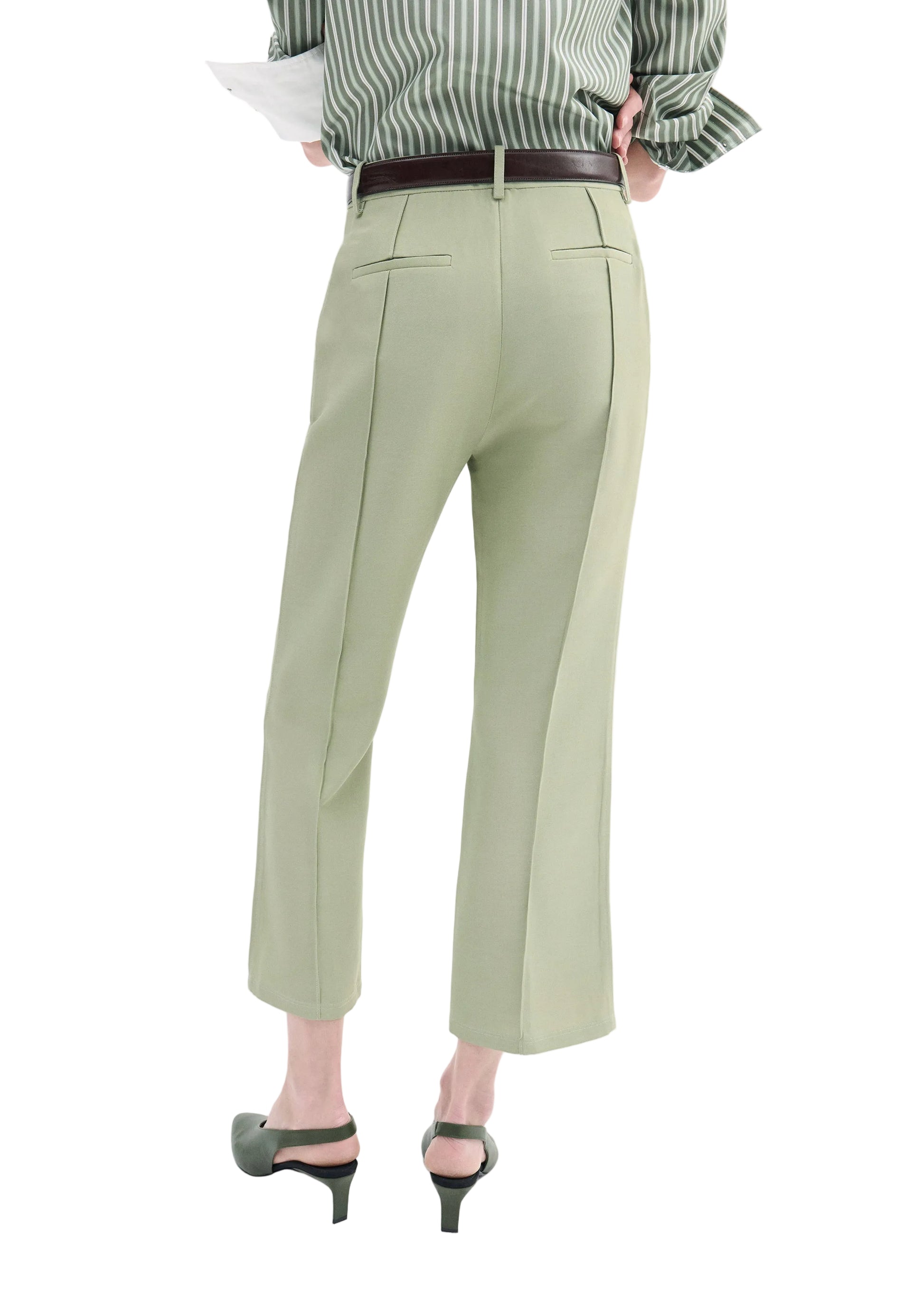 Person wearing CO's Cropped Flared Pant in light green virgin wool, paired with a green and white striped shirt, black belt, and black heeled shoes, standing with their back to the camera.
