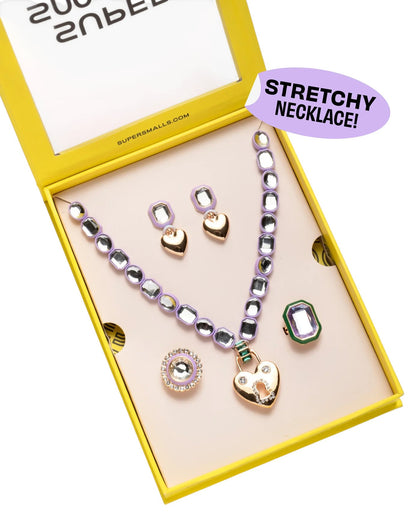 The Super Smalls Lavender Haze Mega Jewelry Set comes in a yellow box with a stretchy purple necklace, earrings, rings, and a heart-shaped pendant, plus a "STRETCHY NECKLACE!" label.