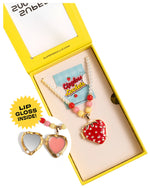 The Super Smalls Strawberry Surprise Lipgloss Locket is a heart-shaped kids’ necklace with a pearl and bead chain in a yellow box. Open the locket to reveal two glossy Strawberry lip gloss shades for fun beauty play.