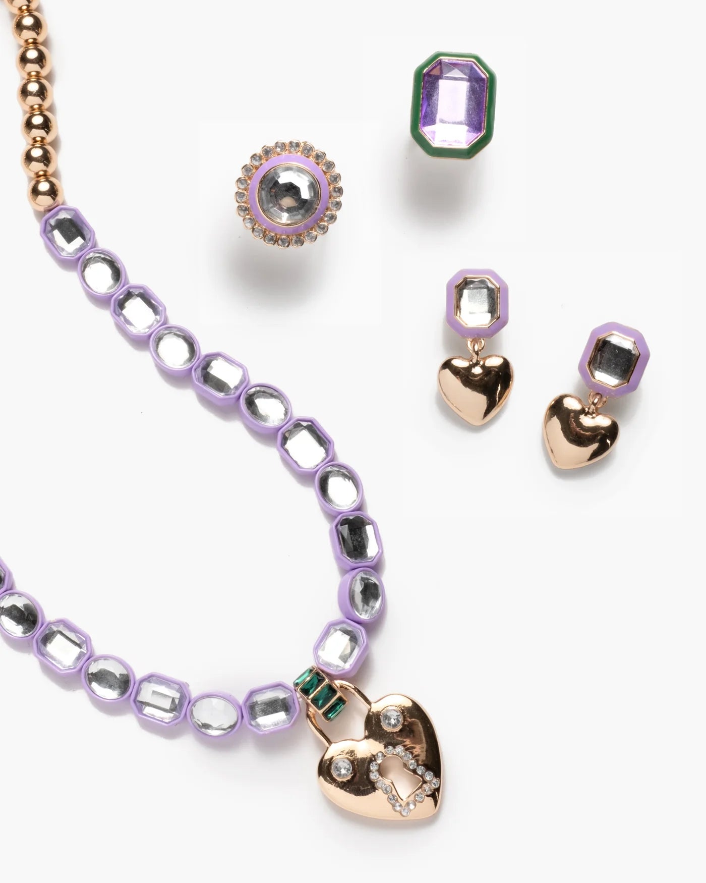 The Super Smalls Lavender Haze Mega Jewelry Set features a purple necklace with gold beads and a heart pendant, a green-bordered ring, plus matching heart-shaped and hexagonal earrings.