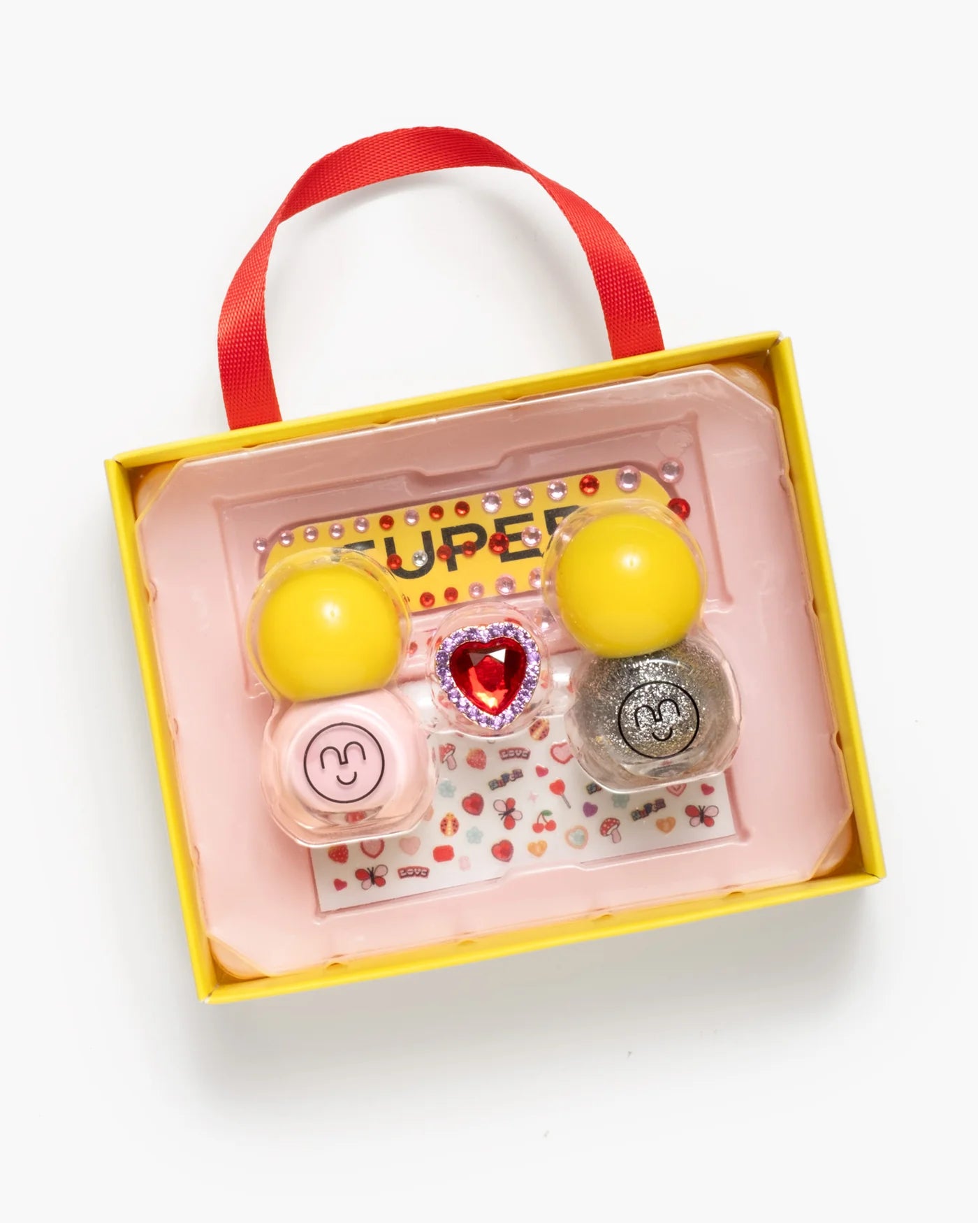 The Super Smalls Paint it Heartfelt Mini Nail Kit includes two yellow-capped bottles, a heart gem, glittery polish, and heart nail stickers, all in a tray with a red handle.