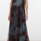 A woman wearing the Staud Albee Dress, an organza sleeveless gown with a floor-length, sheer silhouette and an abstract blue, brown, and red pattern, styled with black sandals and finished with an interior slip for coverage.