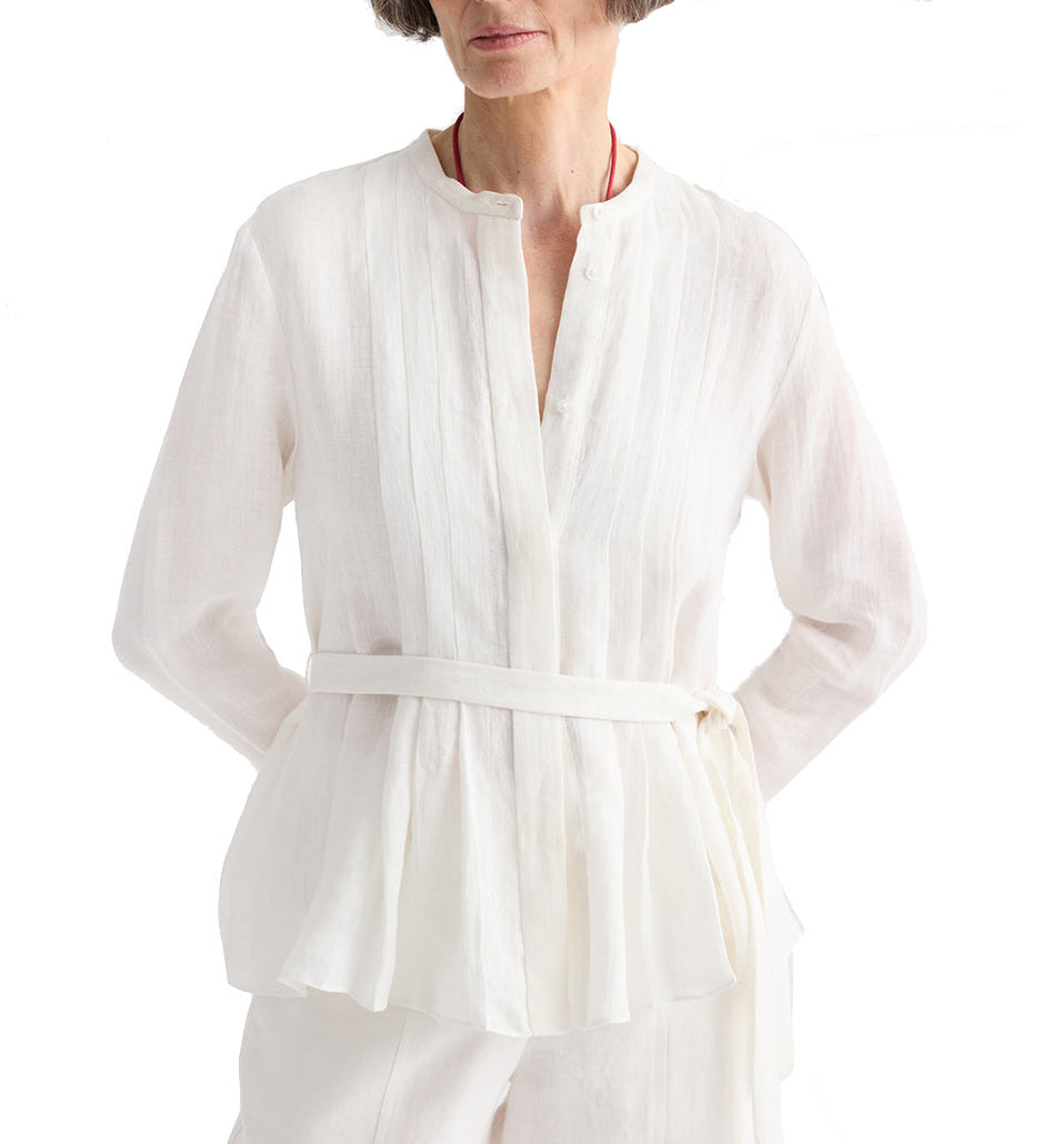 A woman wears the TWP Pleated Poet Blouse, a white linen top with gathered detailing, paired with matching pants. She stands with hands on hips against a plain white background.