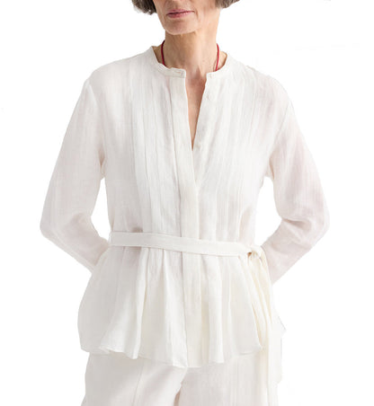 A woman wears the TWP Pleated Poet Blouse, a white linen top with gathered detailing, paired with matching pants. She stands with hands on hips against a plain white background.