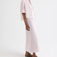 A person wearing the TWP Tie One On Stripe Shirt—a light pink, collared, cotton short-sleeve button-up with stripes—paired with a matching long skirt and brown sandals, stands against a plain white background.