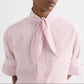 Model wears the TWP Tie One On Stripe Shirt, a cropped short-sleeve button-down featuring red cotton stripes and a necktie knot detail, with rolled sleeves, shown from shoulders to waist against a plain background.