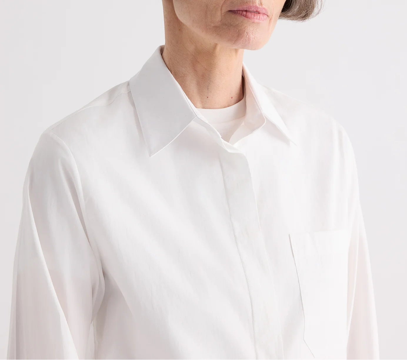 A person wearing the TWP Cowboy Update Shirt, a white collared poplin shirt, shown from shoulders to chest against a plain background.