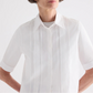 Model wearing the TWP Short Lived Cherry Pleat Top, a white poplin shirt with pintuck detailing on the front, posed against a plain light background.