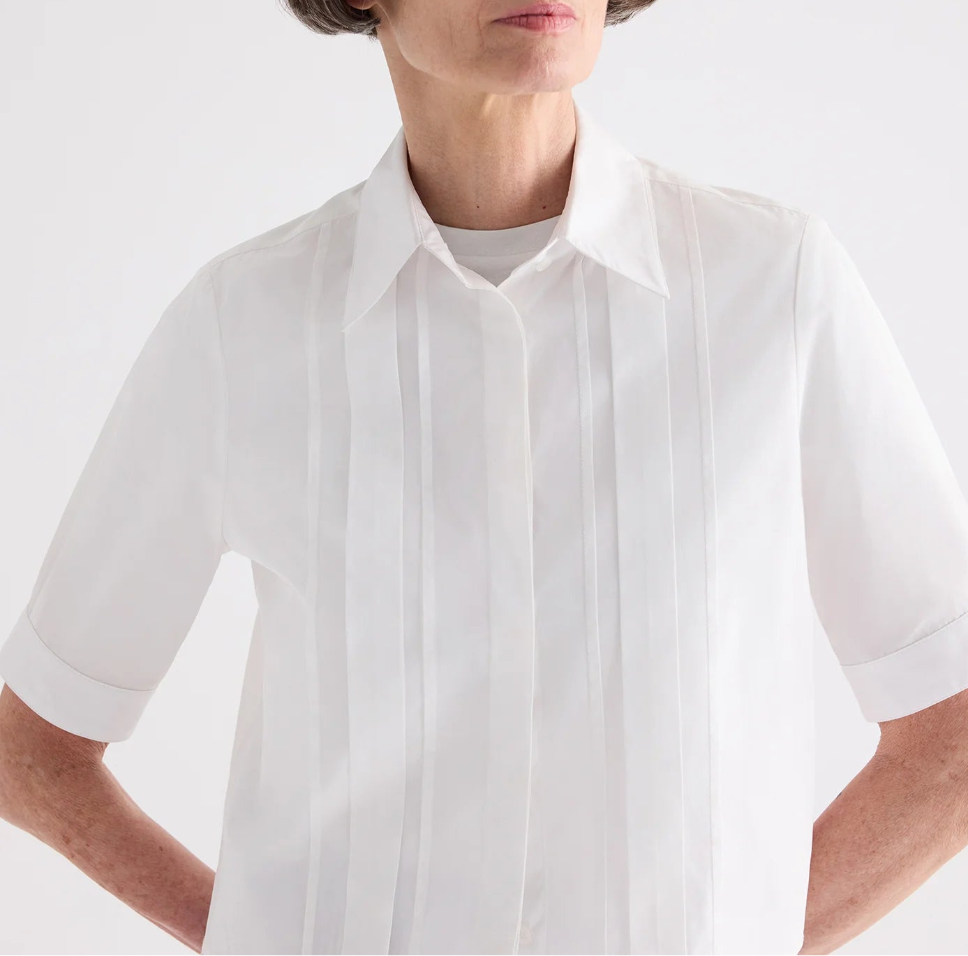 Model wearing the TWP Short Lived Cherry Pleat Top, a white poplin shirt with pintuck detailing on the front, posed against a plain light background.