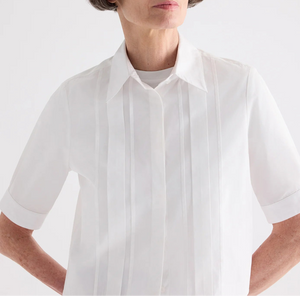 Model wearing the TWP Short Lived Cherry Pleat Top, a white poplin shirt with pintuck detailing on the front, posed against a plain light background.