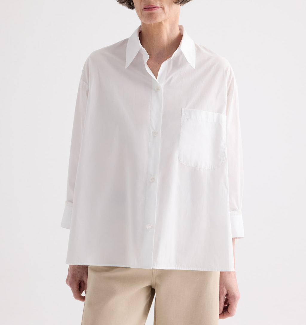 Model wears the TWP Newest Earl Shirt—an oversized button-down crafted from superfine cotton with a chest pocket—styled with light-colored pants and posed against a plain background.