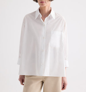 Model wears the TWP Newest Earl Shirt—an oversized button-down crafted from superfine cotton with a chest pocket—styled with light-colored pants and posed against a plain background.