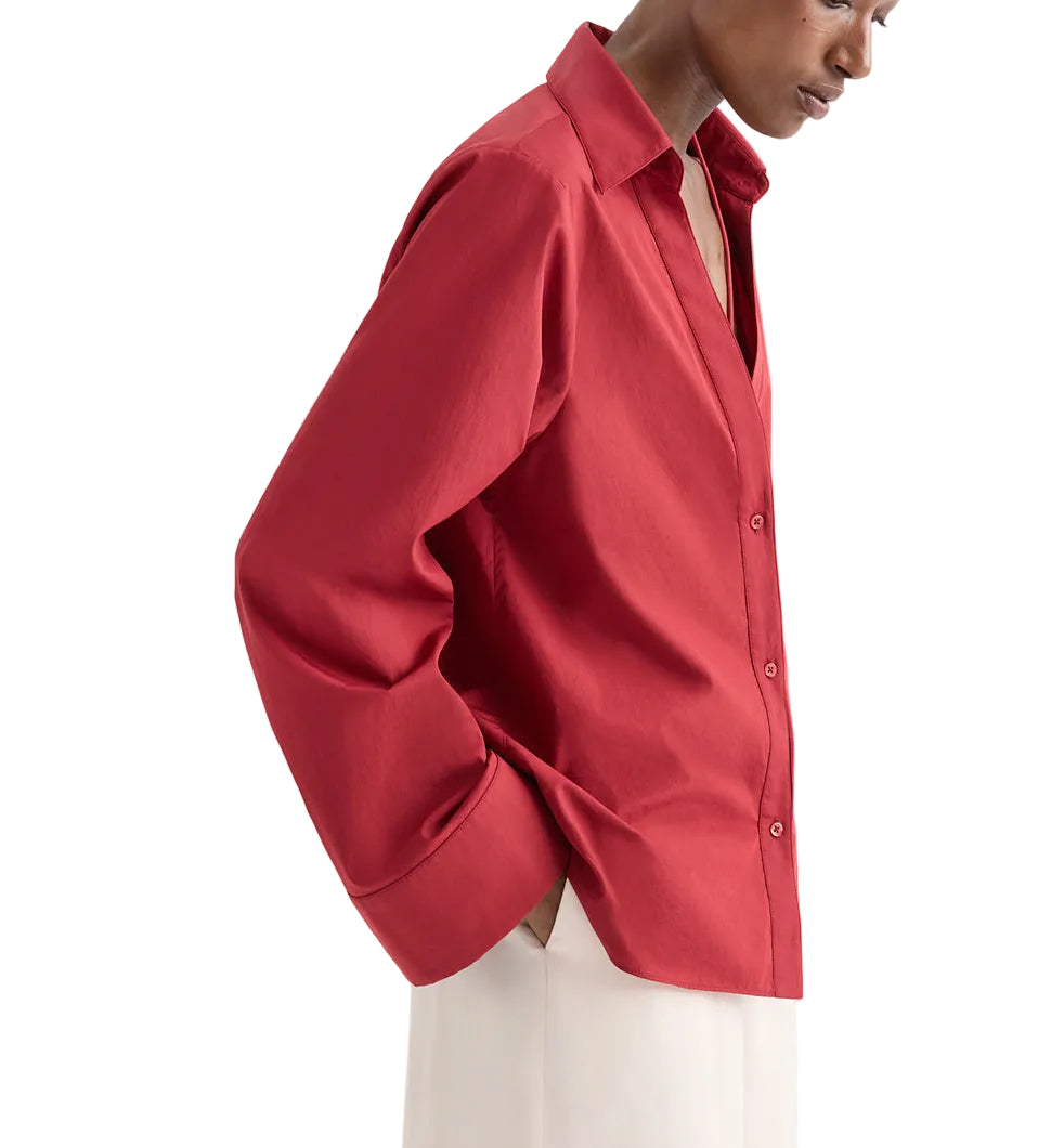 A person wears the Deep V Relaxed Shirt by TWP, crafted from Italian superfine cotton in Karanda Red, paired with off-white pants and standing against a plain background.