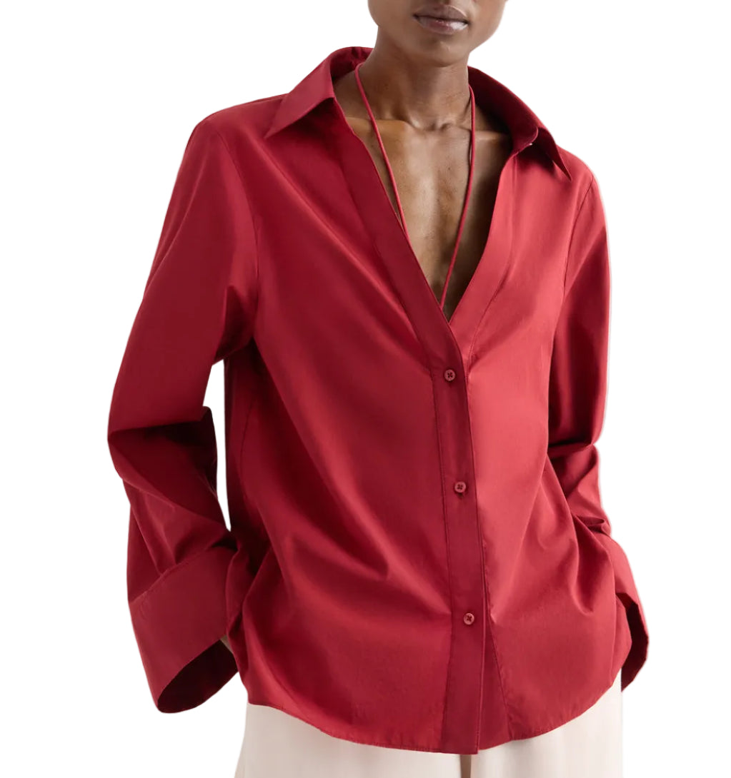 Model wearing the Deep V Relaxed Shirt by TWP in Karanda Red, crafted from Italian superfine cotton. The oversized button-down features an open collar and long sleeves, paired here with light-colored pants. Hands are in pockets and face is partially out of frame.