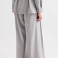 A person is photographed from the back against a plain background, wearing TWP’s Avery Wool Flannel Pant—a light gray, mid-rise, wide-leg style—paired with brown sandals and a loose-fitting suit.