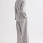 A person stands with their back to the camera, wearing the TWP Tamzin Jacket in Light Heather Grey wool flannel, belted at the waist, paired with matching wide-leg pants and brown sandals, set against a plain white background.