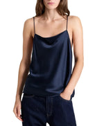 A navy blue crepe back silk satin Sari Tank by TWP featuring a draped cowl neckline and spaghetti straps, worn with dark blue jeans.