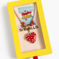 The Strawberry Surprise Lipgloss Locket by Super Smalls is a kids’ necklace with strawberry lip gloss and pearl-like beads, packaged in yellow and labeled "Lipgloss Lockets"—ideal for beauty play.