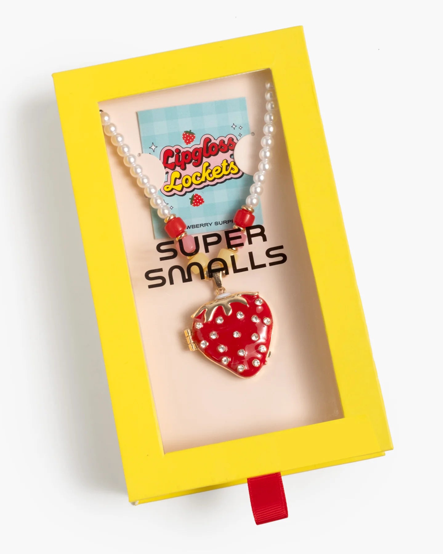 The Strawberry Surprise Lipgloss Locket by Super Smalls is a kids’ necklace with strawberry lip gloss and pearl-like beads, packaged in yellow and labeled "Lipgloss Lockets"—ideal for beauty play.