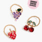 Three gold beaded stretchy rings with grape, cherry, and strawberry designs from Super Smalls’ Gloss it Fruity Lip Gloss Ring Set are displayed on a white background. The label reads “Sparkly Stretchy Rings!”.