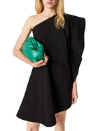 A person wears the Stella McCartney Washed Cotton Asymmetric Mini Dress in black and holds a large green clutch bag.