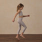 A young girl in Rylee & Cru Girls’ Basic Legging with a leopard print jumps indoors on a wooden floor against a beige background, capturing the energy of everyday flow and effortless class.
