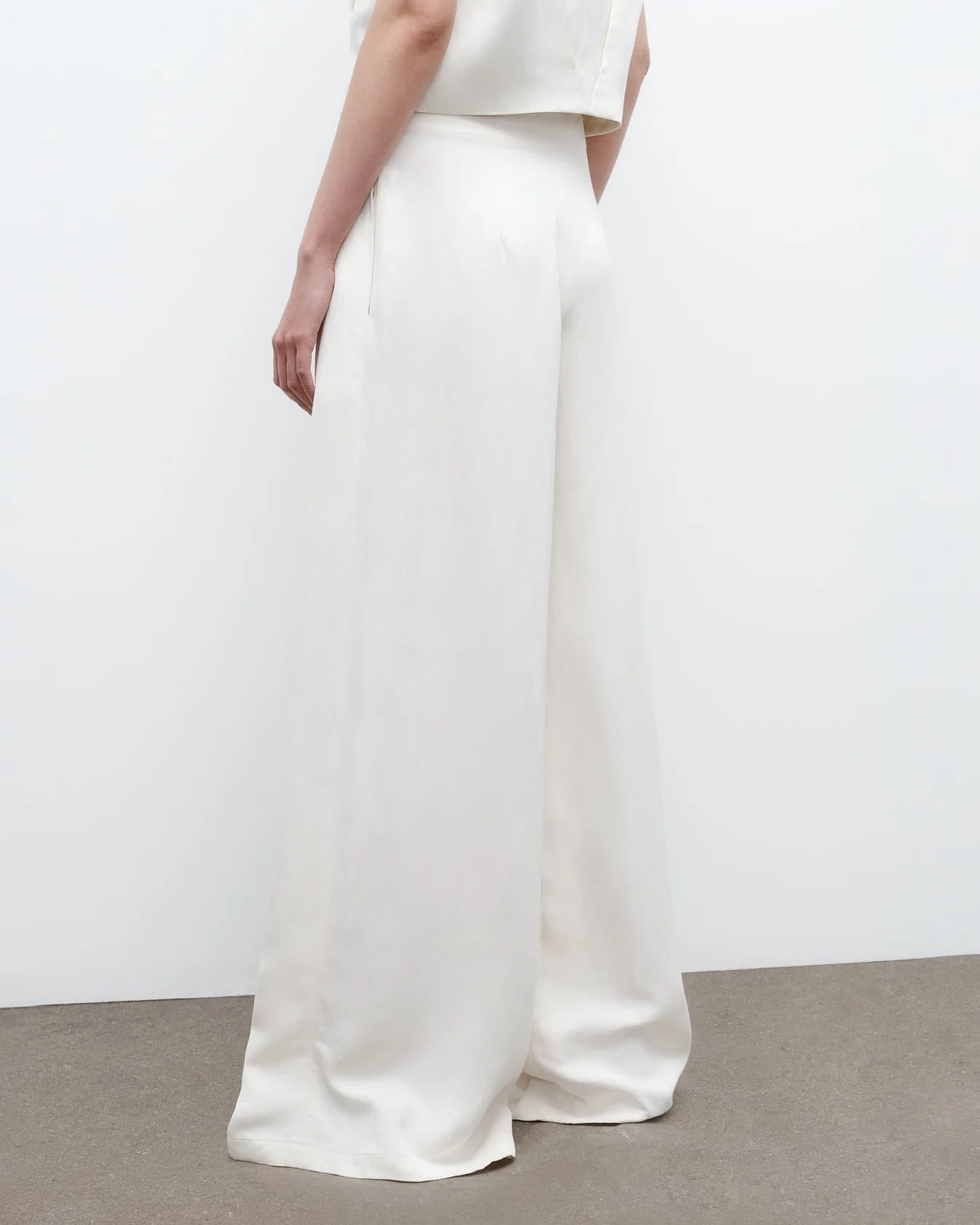 A person wears TWP’s Drew Coated Viscose Linen Pants in white with a sleeveless white top, standing against a plain background.