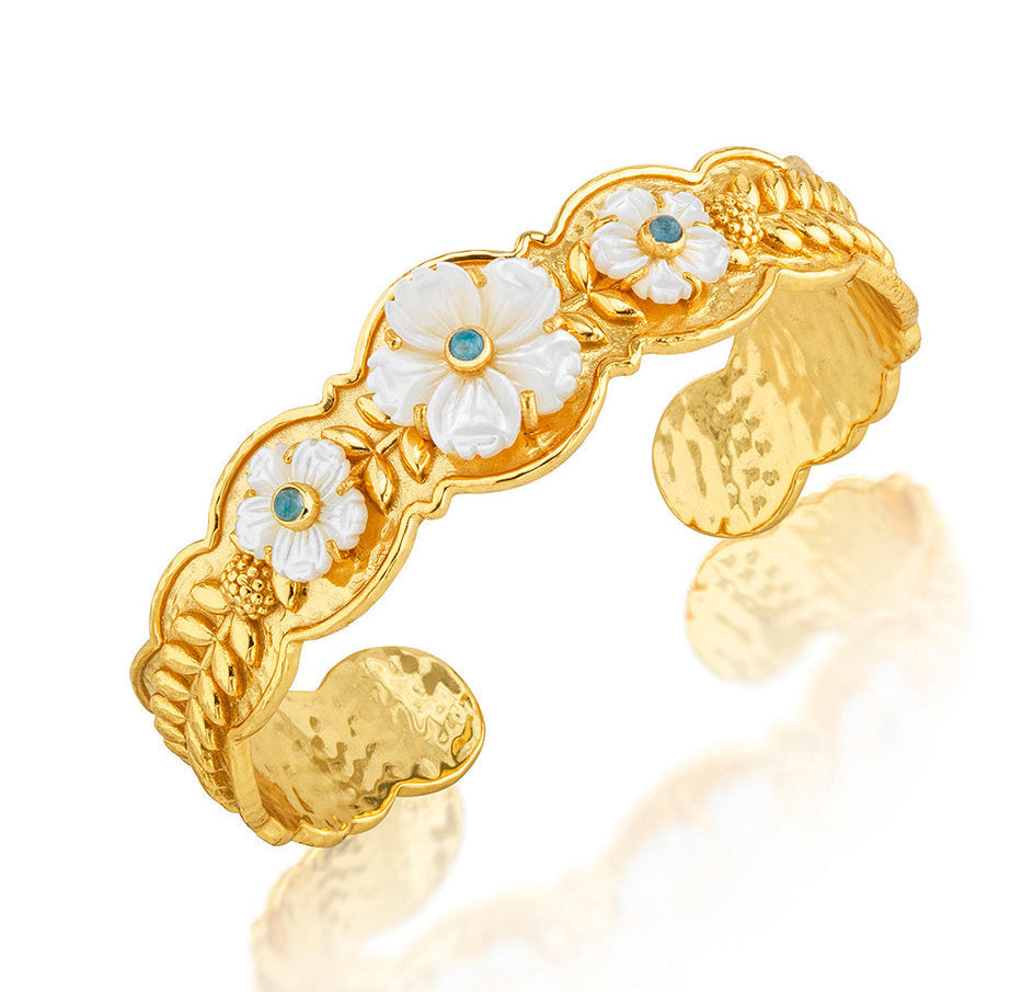 The Villandry Fleur Scalloped Cuff by Juliska Capucine De Wulf features a gold hammered texture, white enamel flowers with blue centers, and intricate leaf details.