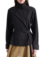 TWP’s The Last Chapter Italian Wool Twill Jacket, featuring a black belted wrap design with high collar, lapels, and button details, styled over a tan skirt.