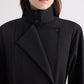 A person is shown from shoulders to mouth wearing TWP’s The Last Chapter Italian Wool Twill Jacket, featuring a high collar, black fabric, an asymmetrical front, and button detailing.