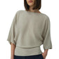 A woman wears the Simkhai Shai Tee, a loose light beige knit with a boxy silhouette, elbow-length sleeves, and wide ribbed waistband, styled with dark jeans.