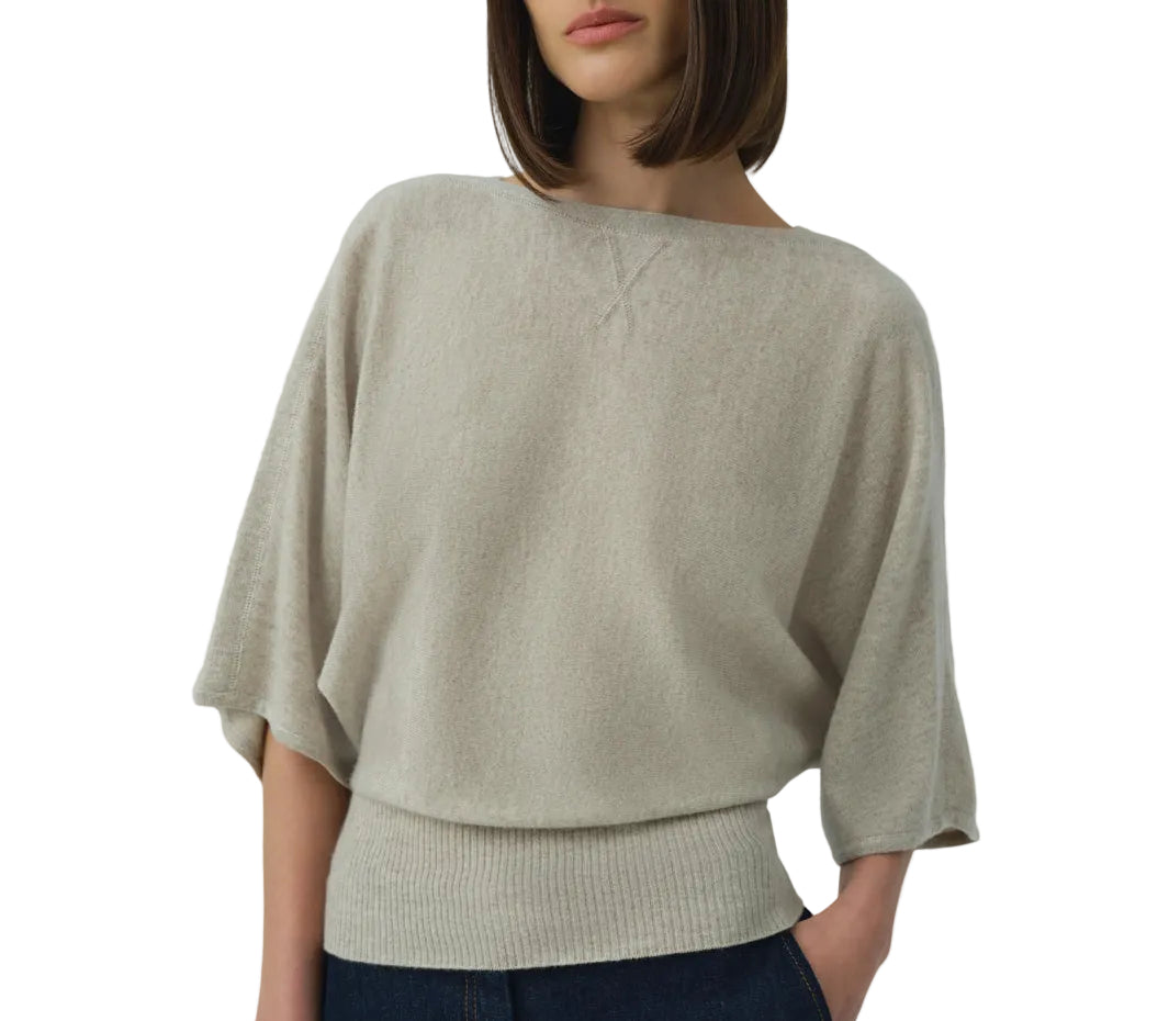 A woman wears the Simkhai Shai Tee, a loose light beige knit with a boxy silhouette, elbow-length sleeves, and wide ribbed waistband, styled with dark jeans.