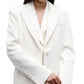 A person wearing the TWP Perfect Boyfriend Blazer—an oversized white single-breasted style with notch lapels and buttoned cuffs—stands against a white background.