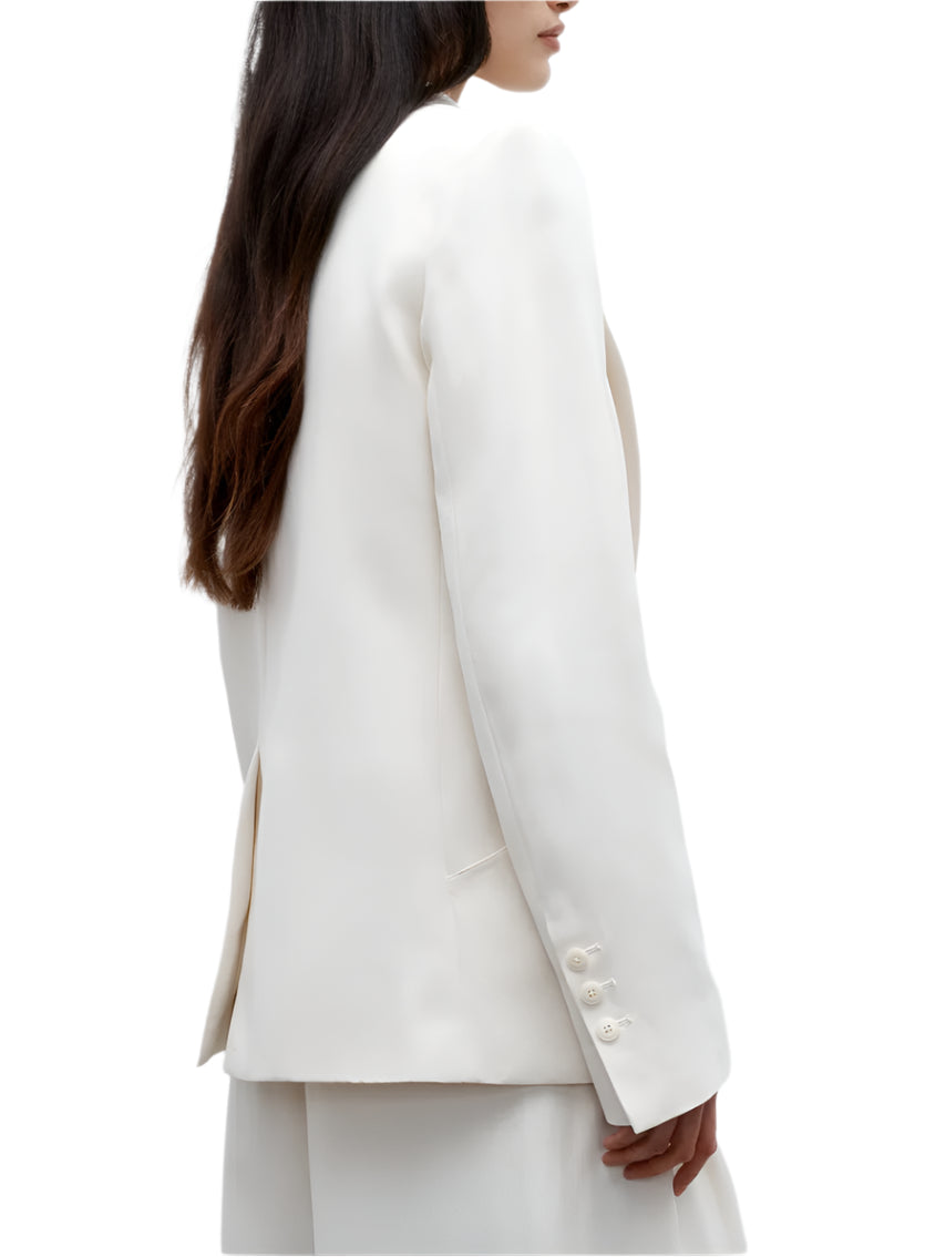 A person in the TWP Perfect Boyfriend Blazer, a white single-breasted style with long sleeves and buttoned cuffs, shown from the side against a white background.