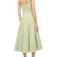 A person is wearing the Wells Dress by Staud, which is light green, sleeveless, calf-length, and fitted. They pair it with sandals while standing against a plain white background.